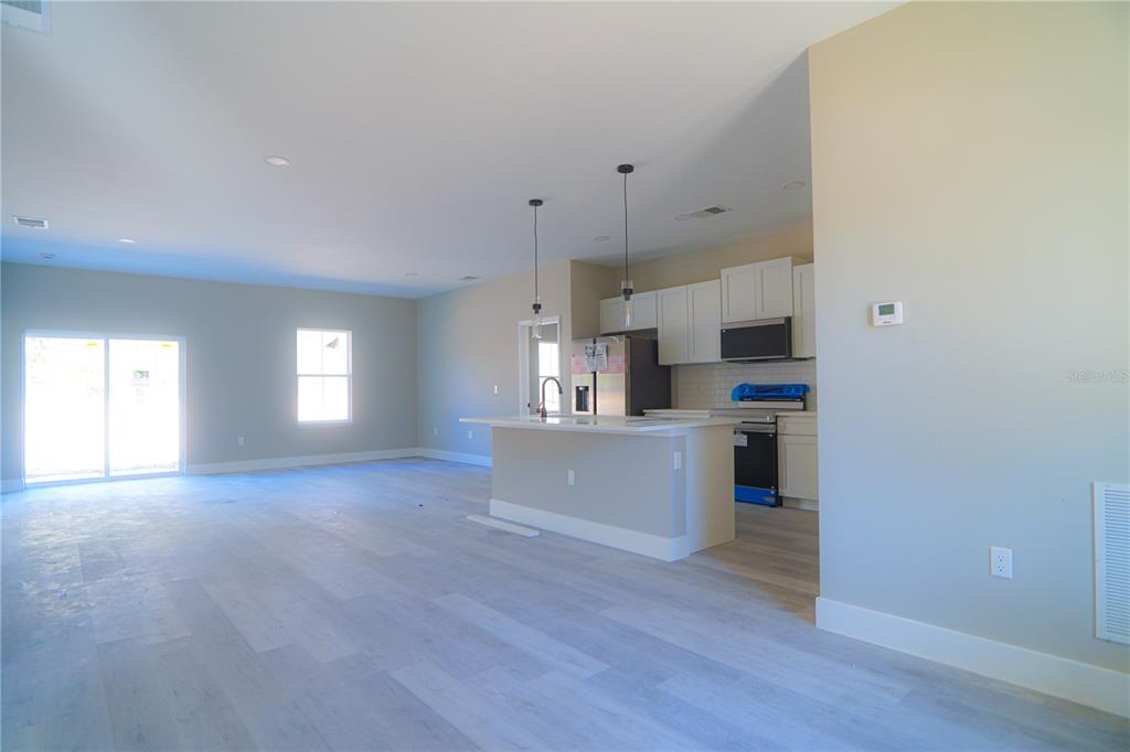 An open-concept kitchen and living area feature light wood-look flooring and white cabinetry — 8413 SW 131ST LANE, OCALA, FL