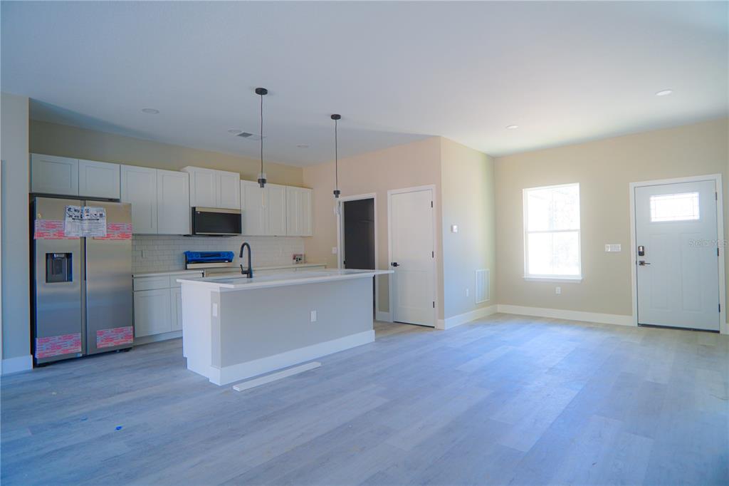 An open-concept living area features light wood-look flooring, beige walls, and a kitchen island — 8413 SW 131ST LANE, OCALA, FL