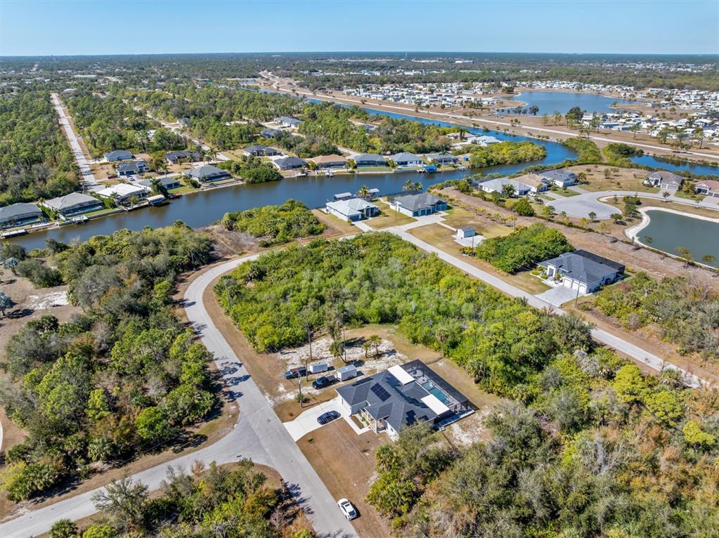 An aerial view shows a residential neighborhood with houses, a canal, and wooded lots — 14303 CANDO AVENUE, PORT CHARLOTTE, FL