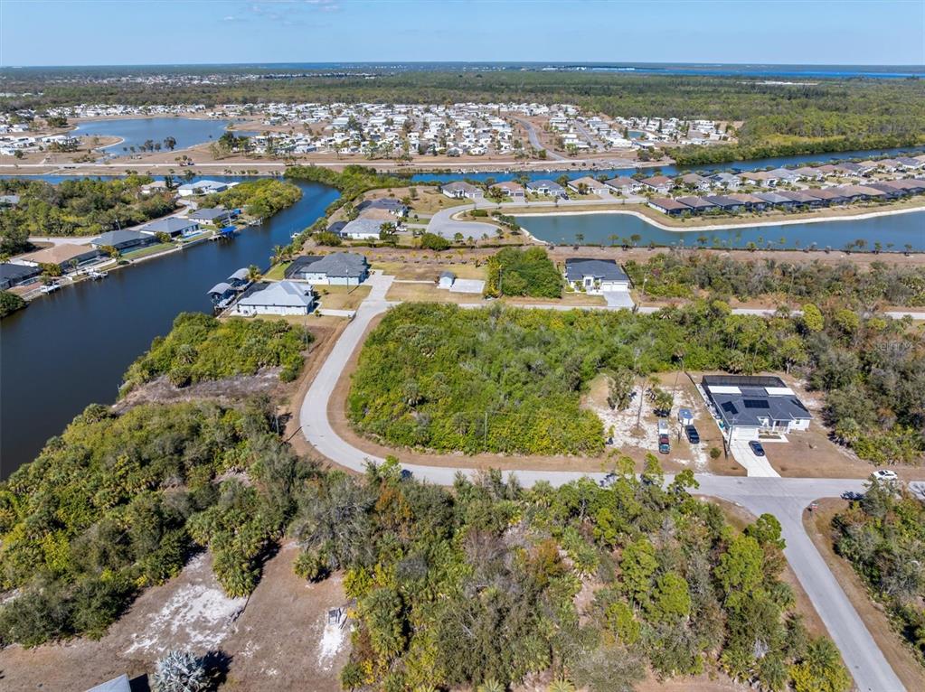An aerial view shows a vacant, wooded residential lot surrounded by houses and canals — 14303 CANDO AVENUE, PORT CHARLOTTE, FL