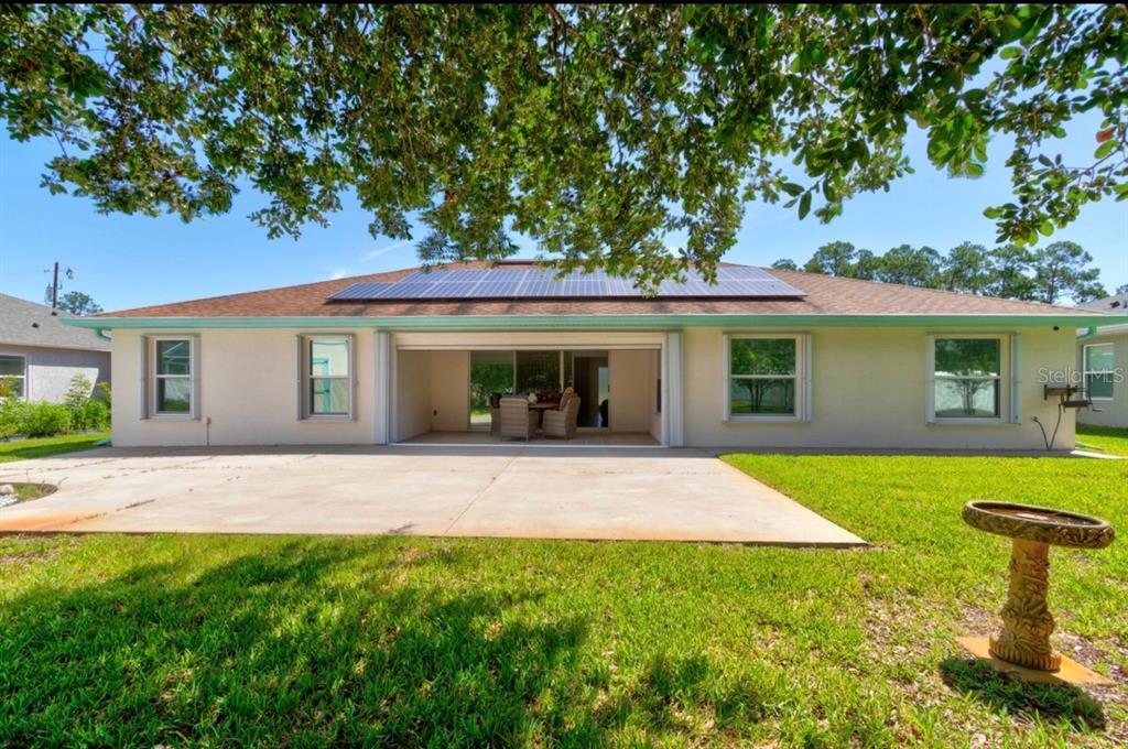 The rear exterior of a single-story house features a concrete patio, solar panels, and lawn — 10 LLOSHIRE PATH, PALM COAST, FL