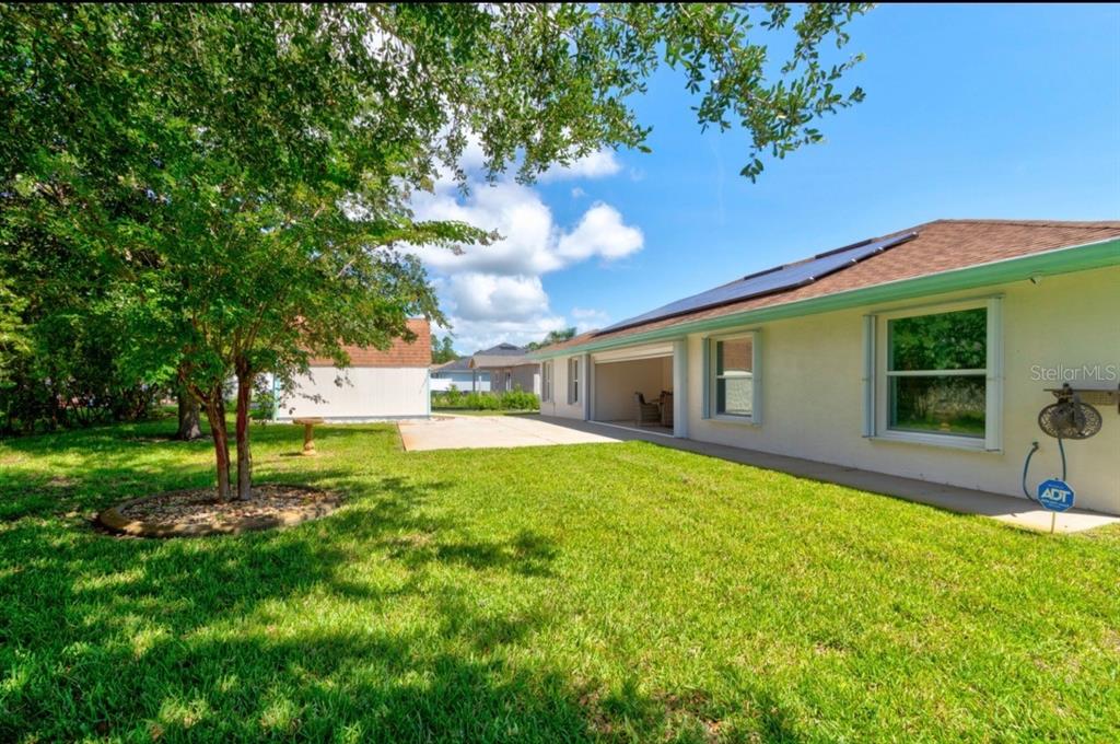 The backyard features a grassy lawn, a concrete patio, and a house with solar panels — 10 LLOSHIRE PATH, PALM COAST, FL