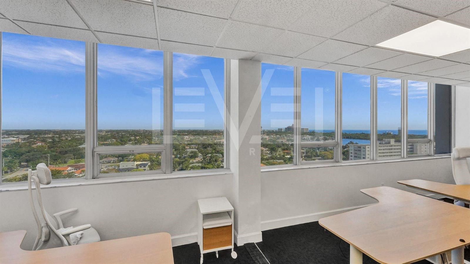 An office space features large windows with panoramic views, light wood desks, and black carpeting — FORT LAUDERDALE, FL