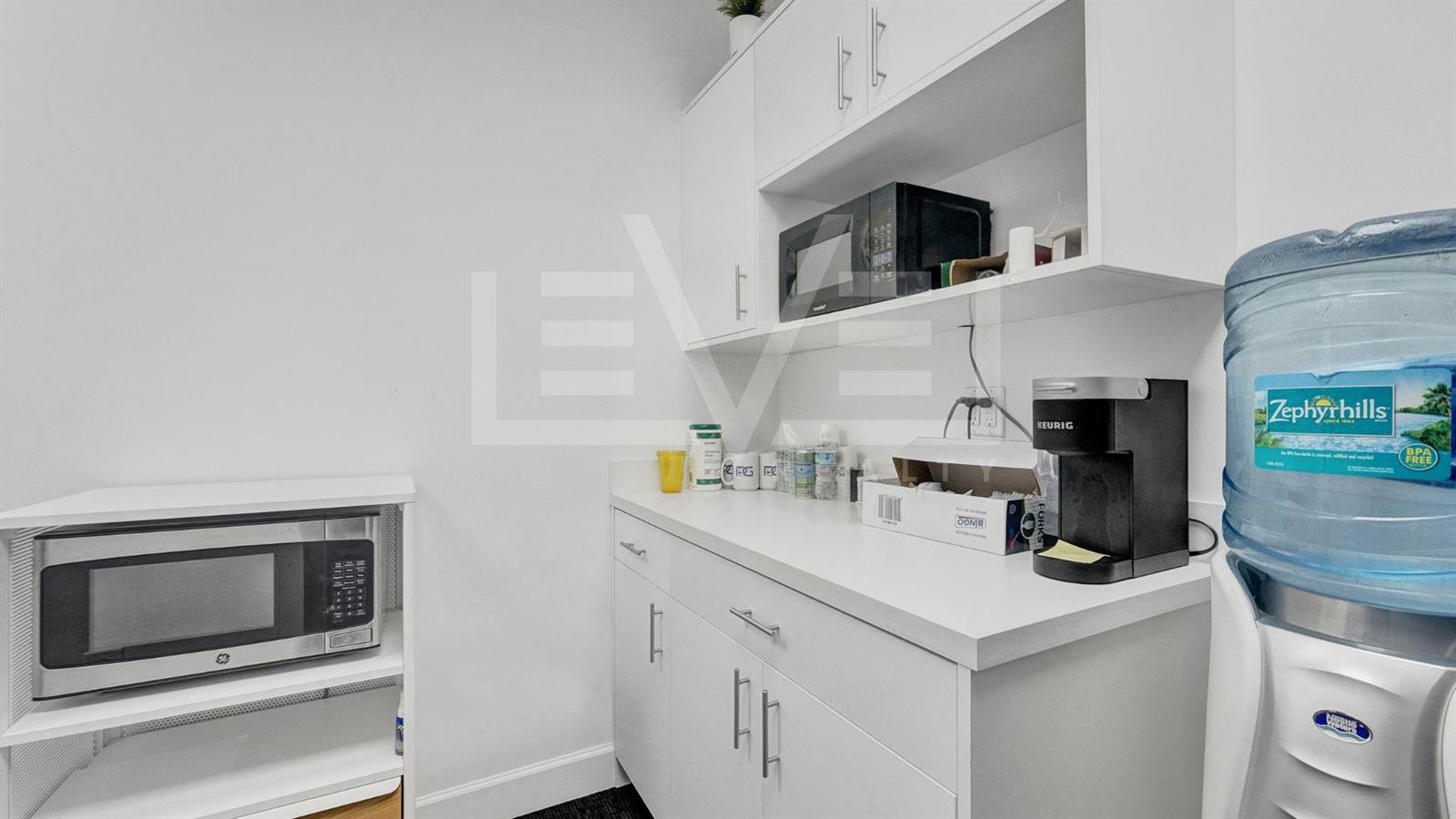 A small office kitchenette features white cabinetry, two microwaves, a coffee maker, and water cooler — FORT LAUDERDALE, FL