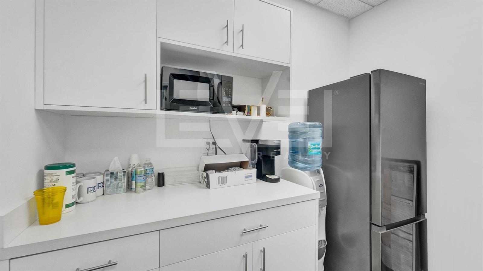 A small office kitchenette features white cabinetry, a microwave, a coffee maker, and a refrigerator — FORT LAUDERDALE, FL