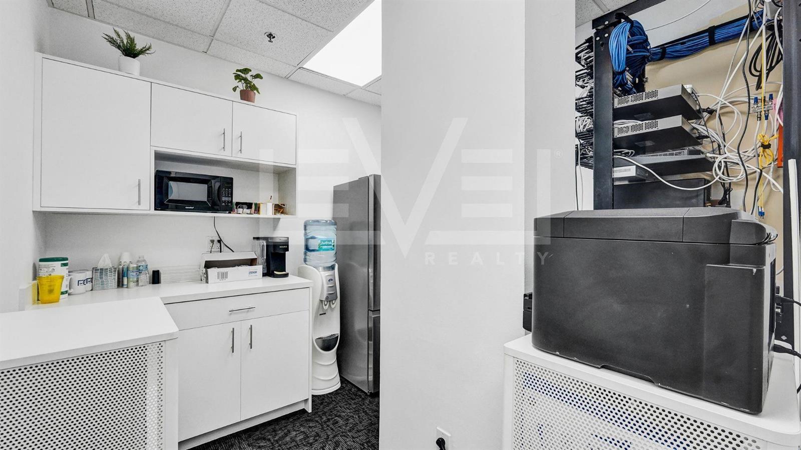 A small office break area features white cabinetry, a microwave, a water cooler, and networking equipment — FORT LAUDERDALE, FL