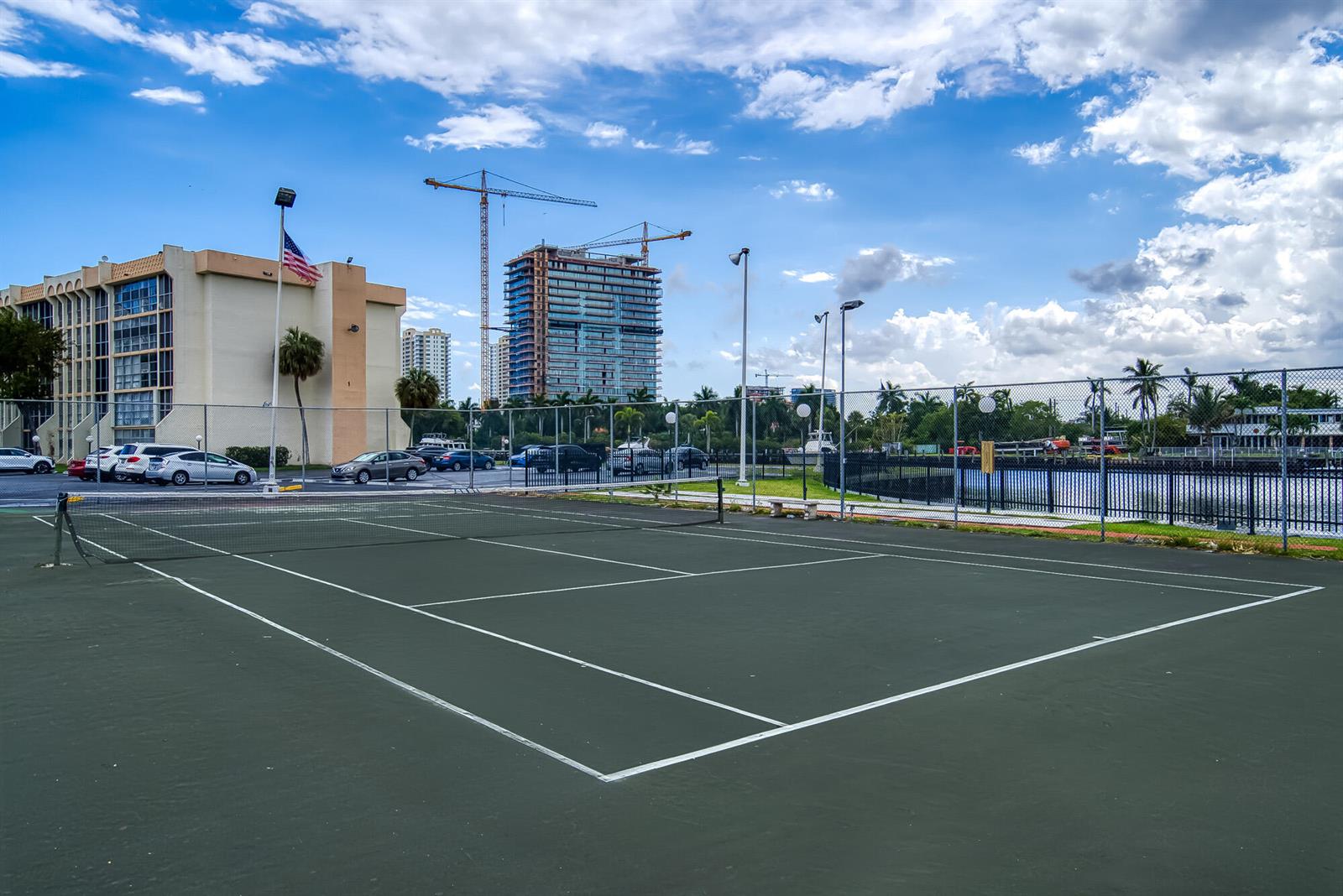 A tennis court sits in the foreground with a parking lot and construction cranes behind — 2000 Atlantic Shores Boulevard # 410, Hallandale Beach FL 33009, HALLANDALE BEACH, FL