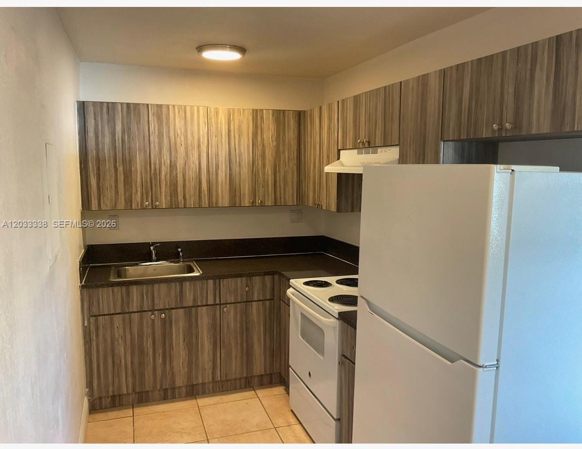 A kitchen features wood-grain cabinets, dark countertops, white appliances, and light-colored floor tiles — 6780 SW 44th St # 2, Miami FL 33155, MIAMI, FL