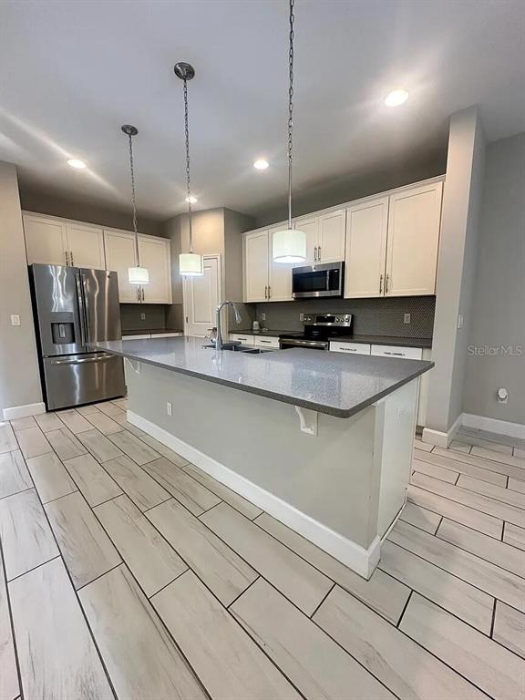 A kitchen features white cabinets, a gray island countertop, stainless steel appliances, and wood-look tile flooring — 534 LAKE WILDMERE COVE, LONGWOOD, FL
