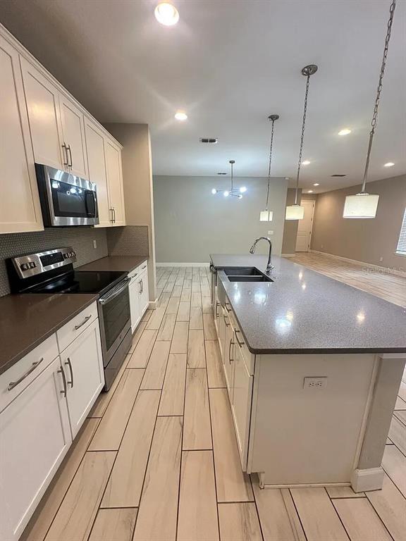A modern kitchen features white cabinetry, a gray island with a sink, and wood-look tile flooring — 534 LAKE WILDMERE COVE, LONGWOOD, FL