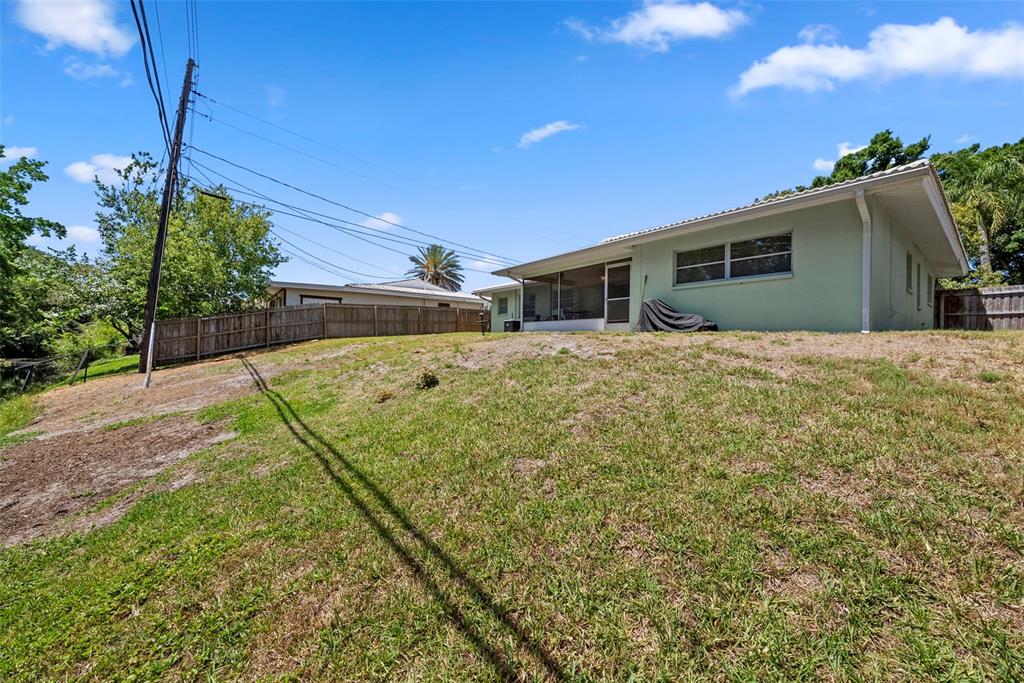 A narrow, dark canal flows alongside a grassy bank lined with dense green trees — 1413 EMBASSY DRIVE, CLEARWATER, FL