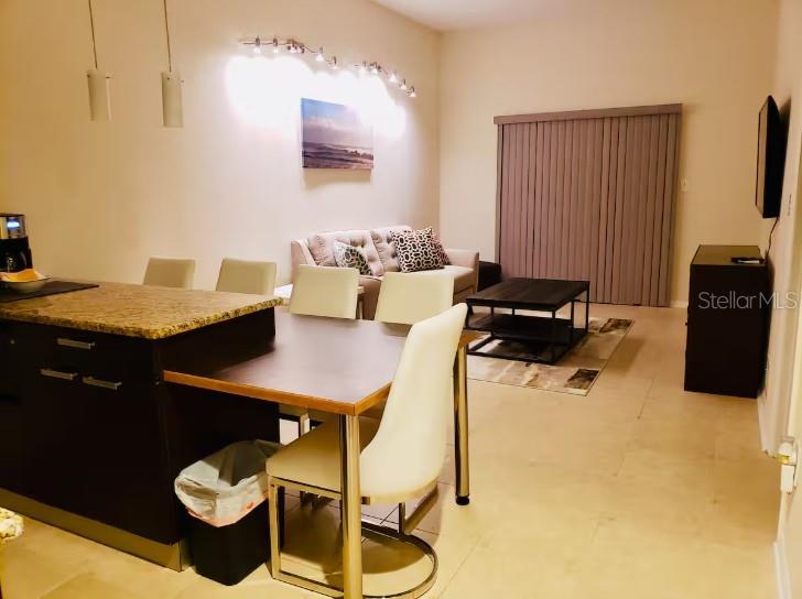 A dining area with a kitchen island and chairs sits before a living room space — 701 S MADISON AVENUE UNIT 109, CLEARWATER, FL
