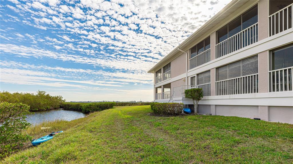 A multi-story building with screened balconies sits beside a grassy lawn and a small canal — 1109 EDGEWATER CIRCLE UNIT 1109, BRADENTON, FL