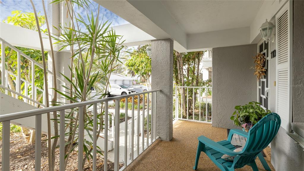 A covered balcony features a teal Adirondack chair, white railings, and a view of landscaping — 1109 EDGEWATER CIRCLE UNIT 1109, BRADENTON, FL