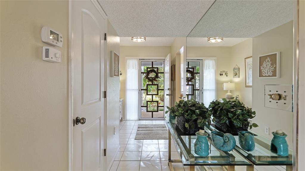 A tiled entryway features a glass-topped console table, a large mirror, and a decorative front door — 1109 EDGEWATER CIRCLE UNIT 1109, BRADENTON, FL