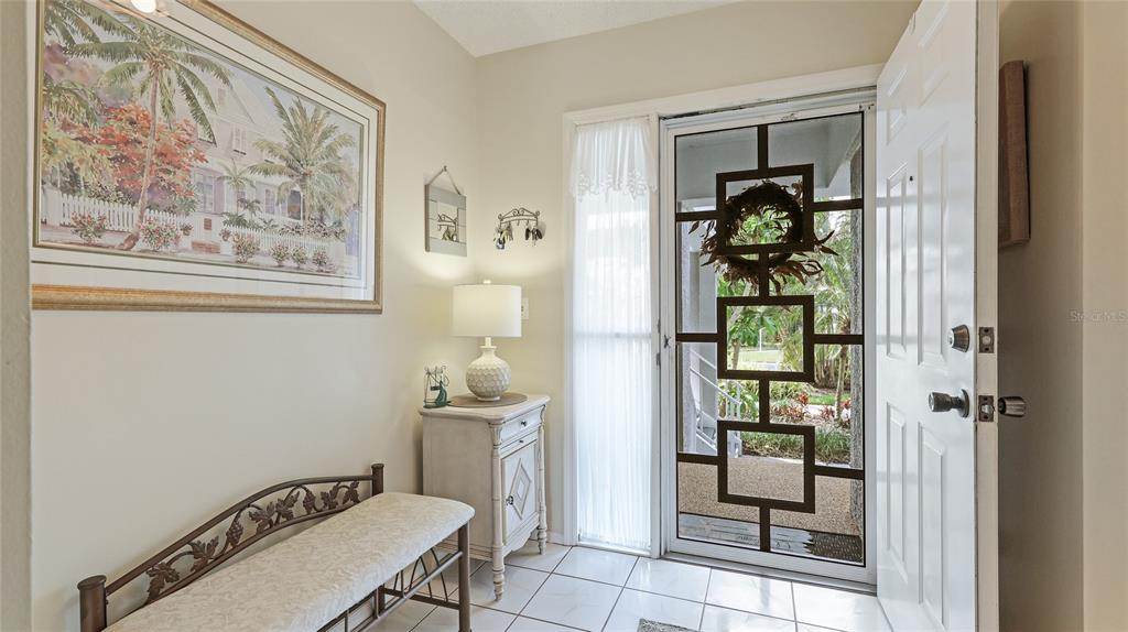 An entryway features a white bench, a small cabinet with a lamp, and a screen door — 1109 EDGEWATER CIRCLE UNIT 1109, BRADENTON, FL