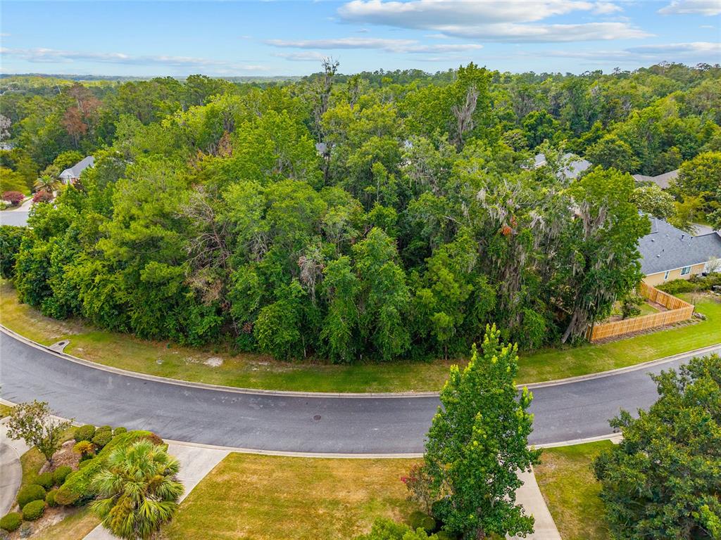 An aerial view shows a vacant, wooded residential lot situated along a curved suburban street — 2645 NW 106TH WAY, GAINESVILLE, FL