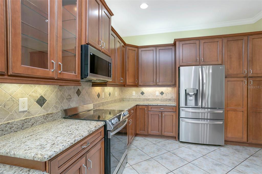 A kitchen features wood cabinets, granite countertops, stainless steel appliances, and tile flooring — 16022 GOLDEN LAKES DRIVE, WIMAUMA, FL