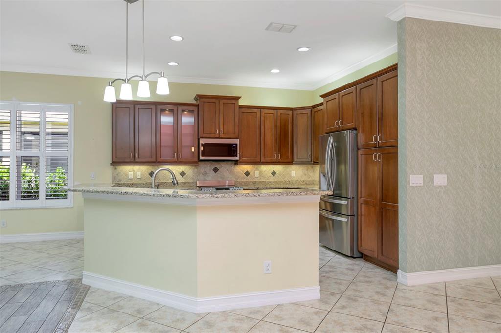 A kitchen features wood cabinets, granite countertops, stainless steel appliances, and tiled flooring — 16022 GOLDEN LAKES DRIVE, WIMAUMA, FL