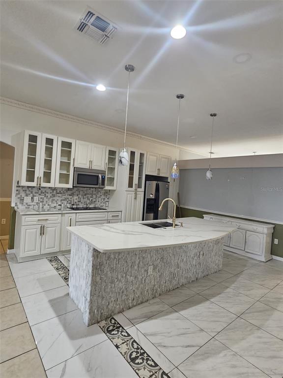 A kitchen features white cabinetry, a large marble-topped island, and light-colored tile flooring — 807 MASSY COURT, KISSIMMEE, FL