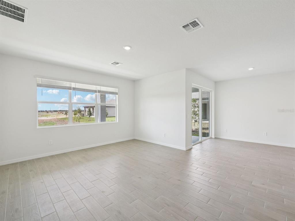 An empty room with light-colored tile flooring, white walls, large windows, and sliding glass doors — 9009 VENETIA COURT, PALMETTO, FL