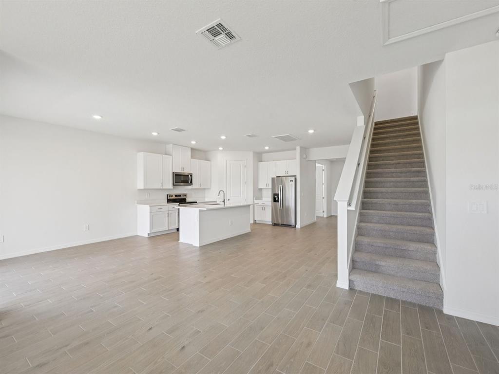 An open-concept kitchen with white cabinetry and an island sits beside a carpeted staircase — 9009 VENETIA COURT, PALMETTO, FL