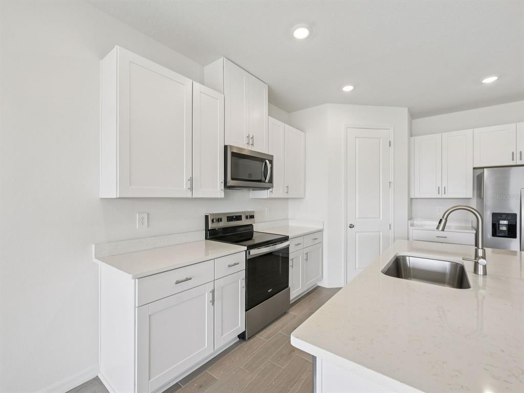 A modern kitchen features white cabinets, stainless steel appliances, and a quartz-topped island — 9009 VENETIA COURT, PALMETTO, FL