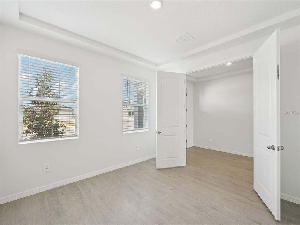 An empty room with white walls, light wood-look flooring, two windows, and open double doors — 9009 VENETIA COURT, PALMETTO, FL