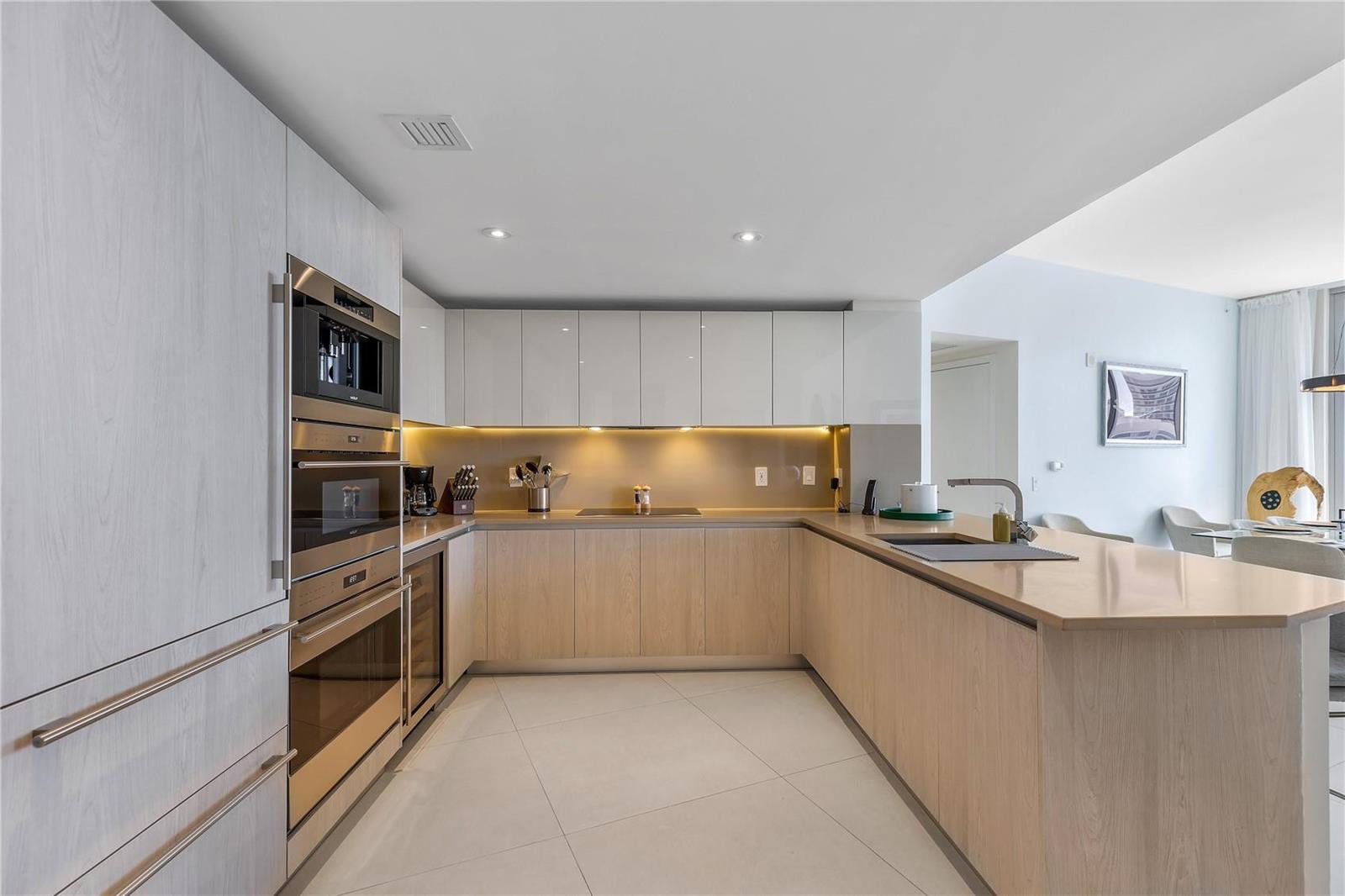A modern kitchen features light wood cabinetry, white upper cabinets, stainless steel appliances, and countertops — 4111 S Ocean Drive, Hollywood FL 33019, HOLLYWOOD, FL