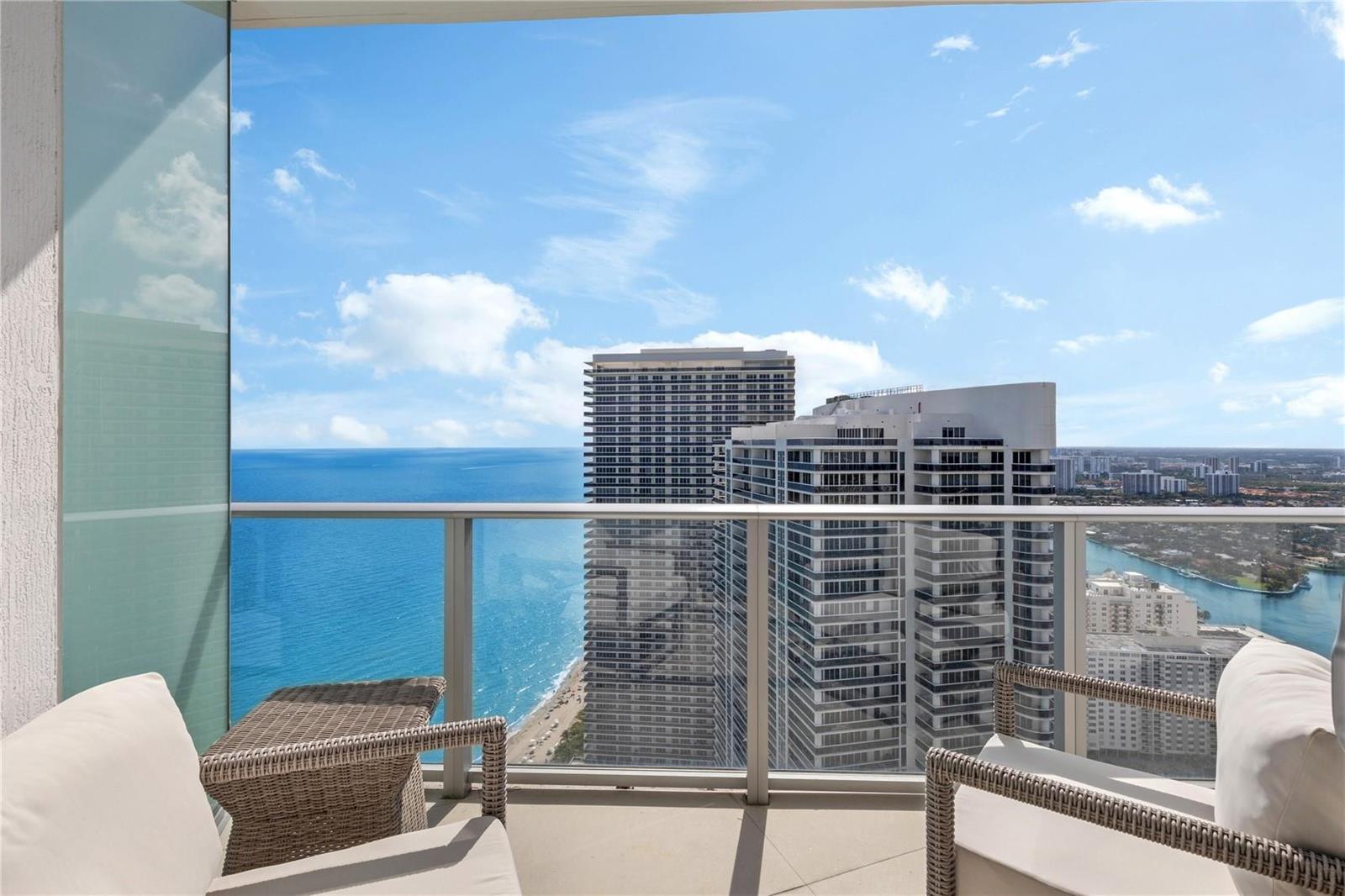 A high-rise balcony with wicker chairs overlooks the ocean and neighboring apartment buildings — 4111 S Ocean Drive, Hollywood FL 33019, HOLLYWOOD, FL