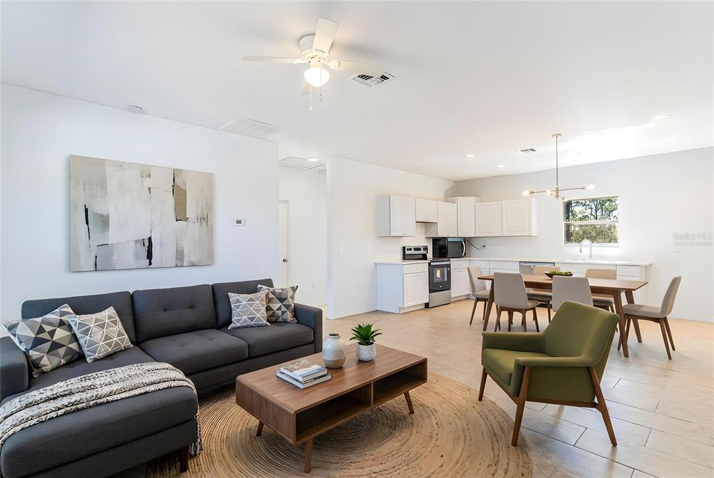 An open-concept living room and kitchen featuring a gray sectional, dining area, and white cabinetry — 1413 BITTERSWEET STREET, LAKE PLACID, FL