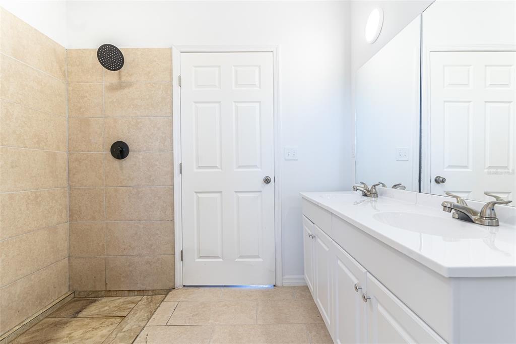 A bathroom features a tiled walk-in shower, a white vanity with dual sinks, and a door — 1413 BITTERSWEET STREET, LAKE PLACID, FL