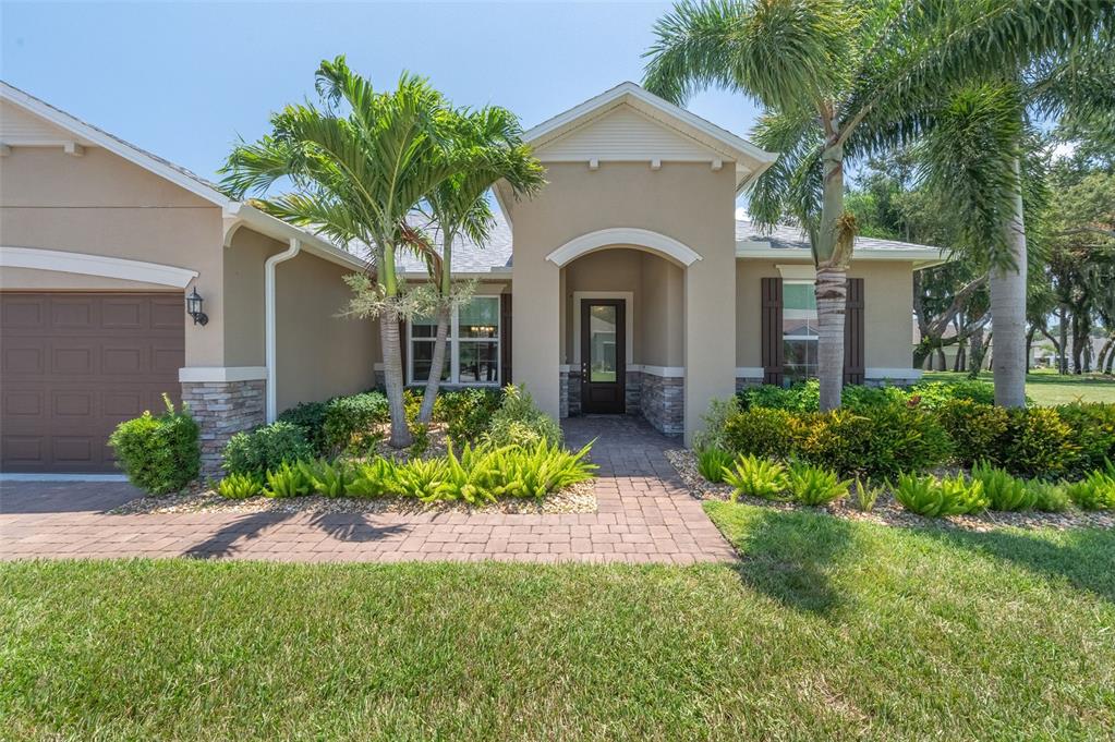 A tan stucco house features a stone-accented entryway, a brown garage door, and palm trees — 2003 KILLIAN DRIVE NE, PALM BAY, FL