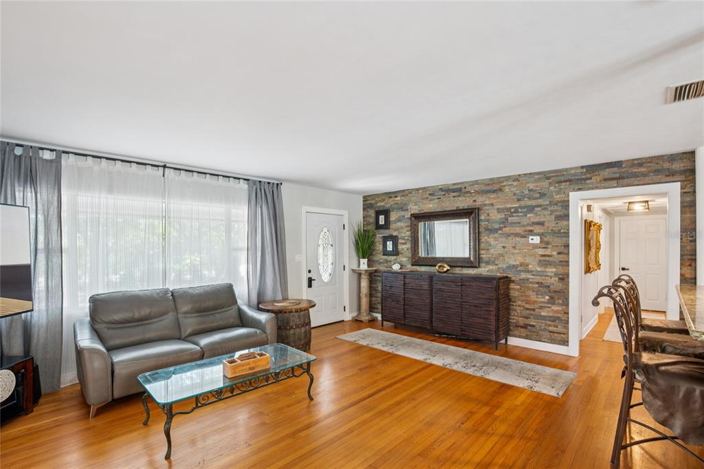 A living room features hardwood floors, a stone accent wall, and a gray leather sofa — 804 WOODRUFF AVENUE, CLEARWATER, FL