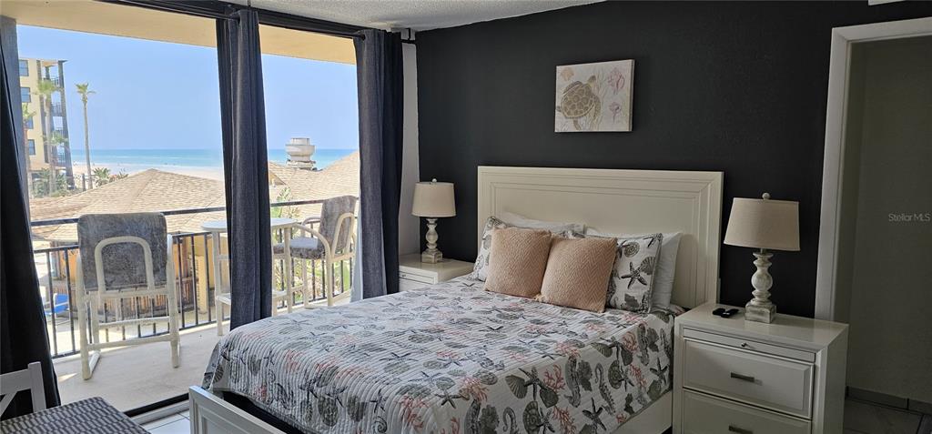 A bedroom with a queen bed, dark accent wall, and a balcony overlooking the ocean — 2301 S ATLANTIC AVENUE UNIT 229, DAYTONA BEACH, FL