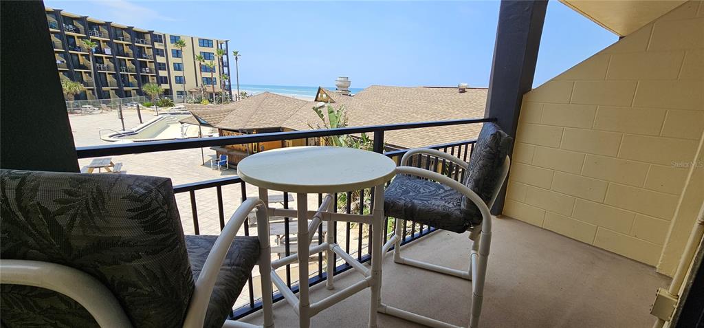 A balcony with a small table and two chairs overlooks a pool area and beach — 2301 S ATLANTIC AVENUE UNIT 229, DAYTONA BEACH, FL