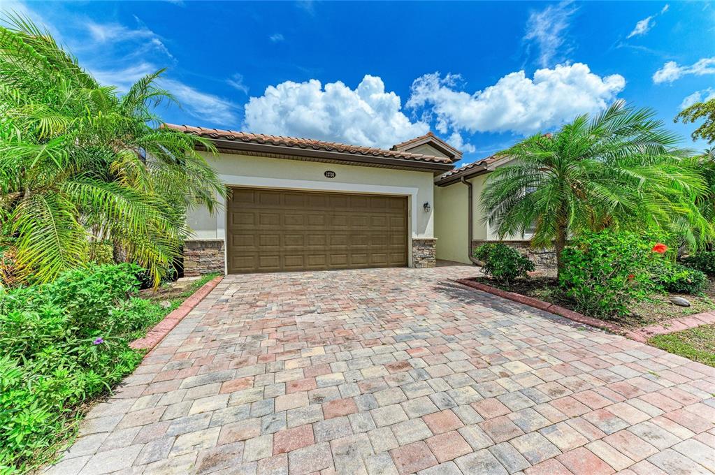 A single-story house with a brown garage door, stone accents, and palm trees in front — 12736 RICHEZZA DRIVE, VENICE, FL