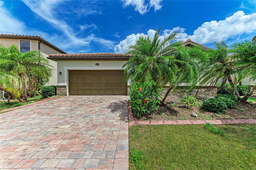 A single-story house with a brown garage door, paver driveway, and palm trees in front — 12736 RICHEZZA DRIVE, VENICE, FL