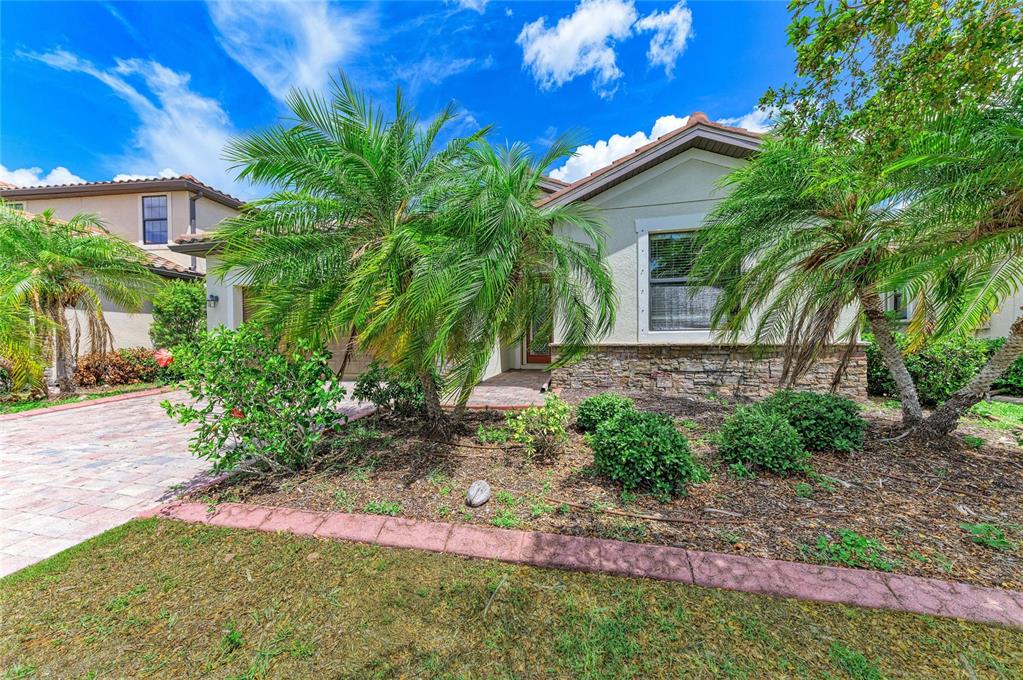 A single-story house with a stone facade, palm trees, and a brick paver driveway — 12736 RICHEZZA DRIVE, VENICE, FL