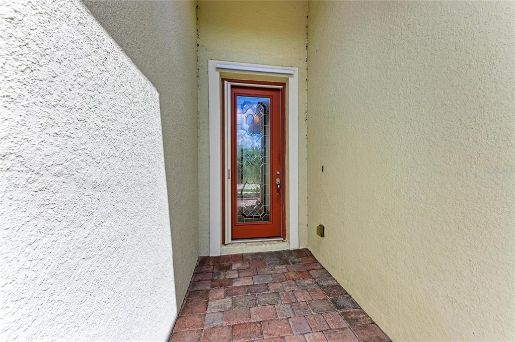 A red front door with a glass insert sits in a recessed entryway with pavers — 12736 RICHEZZA DRIVE, VENICE, FL