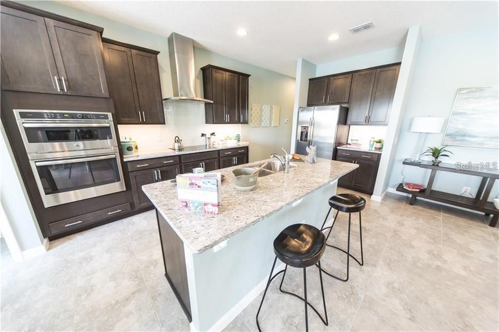 A kitchen features dark wood cabinets, granite countertops, a center island, and stainless steel appliances — 3318 STRATTON CIRCLE, KISSIMMEE, FL