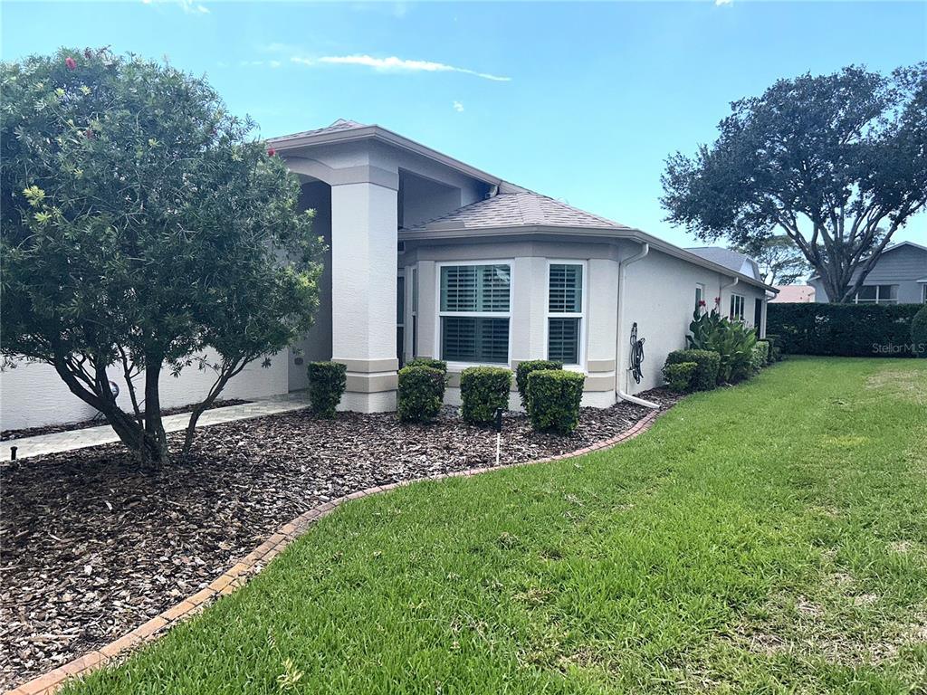 The exterior of a single-story house features a covered entryway, beige stucco, and landscaped lawn — 18505 GRAND CLUB DRIVE, HUDSON, FL