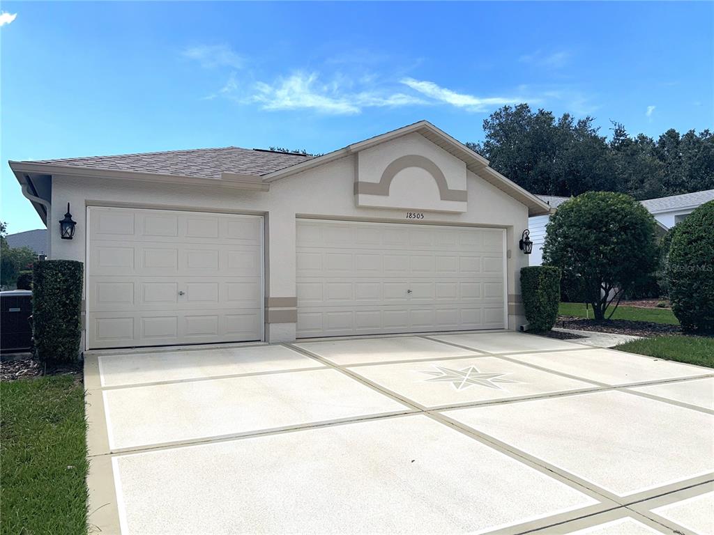 A beige house exterior features a three-car garage and a decorative concrete driveway — 18505 GRAND CLUB DRIVE, HUDSON, FL