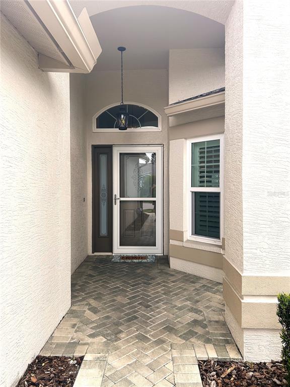 A covered entryway features a brick-paver floor, a glass storm door, and a hanging lantern — 18505 GRAND CLUB DRIVE, HUDSON, FL