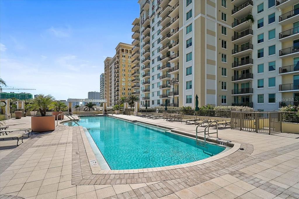 A rectangular swimming pool sits on a paved terrace beside a tall residential building — 800 N TAMIAMI TRAIL UNIT 203, SARASOTA, FL
