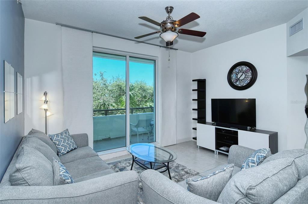 A living room features gray sofas, a glass coffee table, a television, and a balcony — 800 N TAMIAMI TRAIL UNIT 203, SARASOTA, FL