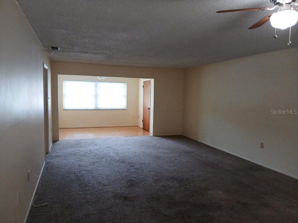 A living room with gray carpet leads to a separate dining area with wood flooring — 7560 92ND STREET UNIT 201B, SEMINOLE, FL