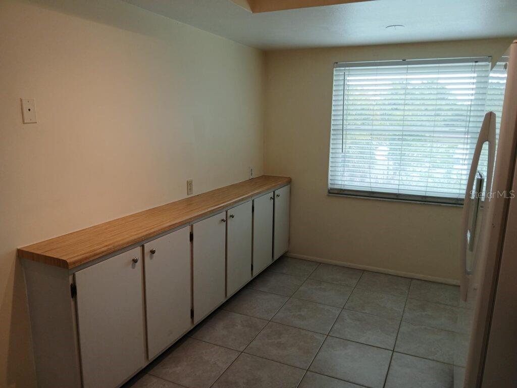 A kitchen features white cabinets, a wood-look countertop, tiled flooring, and a window with blinds — 7560 92ND STREET UNIT 201B, SEMINOLE, FL