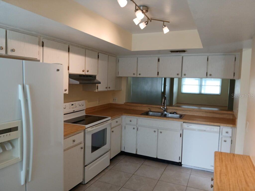 A kitchen features white cabinets, light-colored countertops, a white refrigerator, and a tile floor — 7560 92ND STREET UNIT 201B, SEMINOLE, FL
