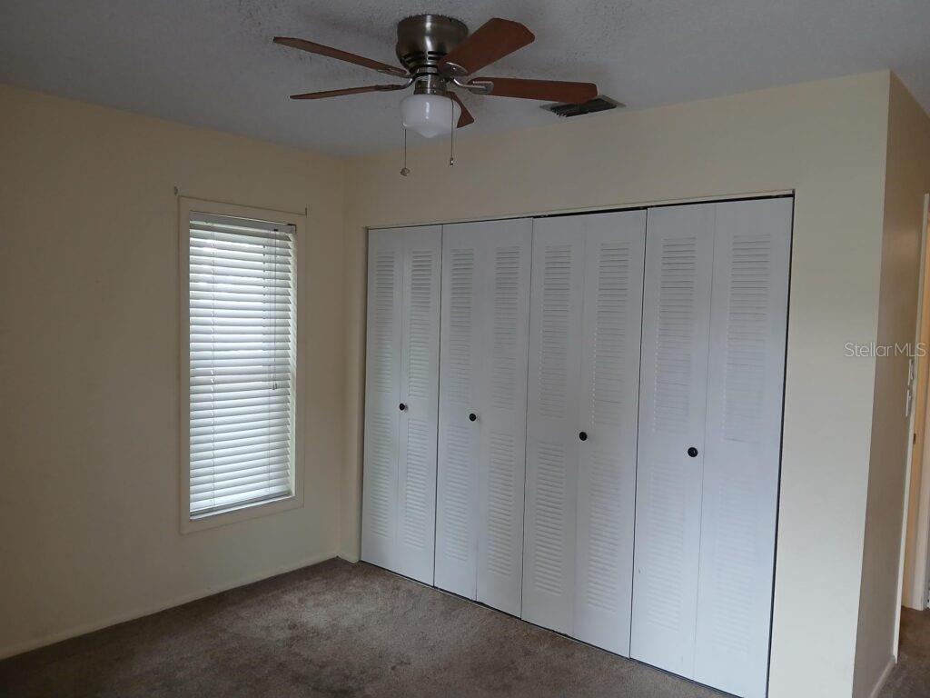A bedroom features beige walls, brown carpet, a ceiling fan, and white louvered closet doors — 7560 92ND STREET UNIT 201B, SEMINOLE, FL